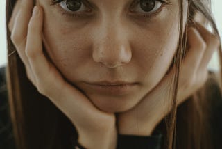 Young girl with long hair and her head cupped in her hands staring out at you looking a bit depressed