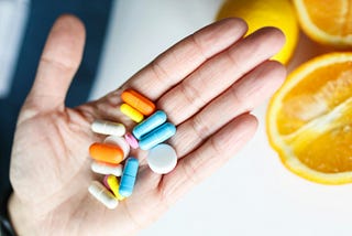 Imagem de mão com vários comprimidos e cápsulas de variadas cores.