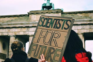 A woman holding a cardboard sign at a rally with the words scientists for future