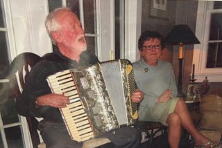 Man playing the accordion and singing with woman sitting beside him