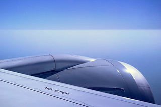 View from an airplane — horizon between sky and clouds, with plane engine in the foreground