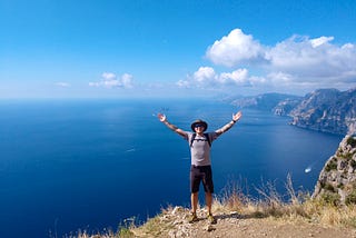 Man with hands stretched out over his head posing in front of the Amalfi Coast.