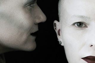 A human or human-like figure appears to whisper something into another human’s ear.