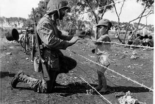 Photo no 127-GW-090935, July 1944 “Give me candy.” Photo of soldier giving candy to child in Tinian.