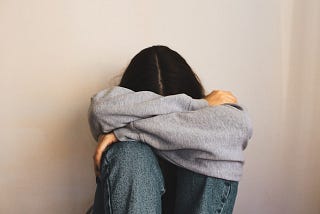Woman sitting on the floor with her knees to her chest and arms wrapped around her head, appearing overwhelmed and isolated — capturing emotions of rejection, loneliness, and feeling left out.