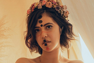 high-key-portrait-of-a-young-topless-woman-with-alternative-makeup-and-face-paint-wearing-a-flower-crown-with-warm-lighting-and-a-dreamy-effect-caused-by-an-intentional-blur