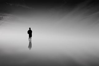 A silhouette of a person standing on the horizon between light and dark.