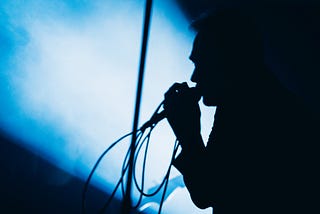 Silhouette of James Reid leaning into mic against blue stagelight and shadow.