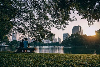 A couple resting on a park bench enjoying the view of skyscrapers in Bangkok.