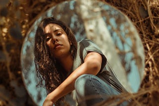 a young woman looking thoughtfully at her reflection in the mirror