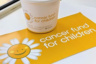 Image of a bucket and poster with a white and yellow Cancer Fund For Children logo