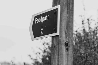 A sign post shaped like a arrow with the word Footpath on it and a figure of a person walking. The sign is angled to the left.