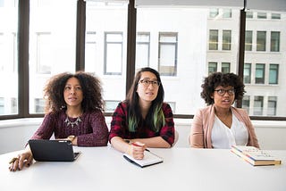 Three women sitting in an office in disbelief