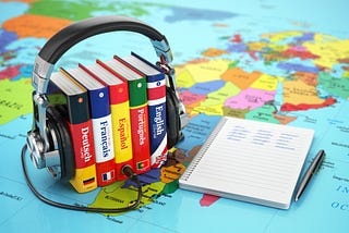 Language books surrounded by headphones and sitting on a map of the world.