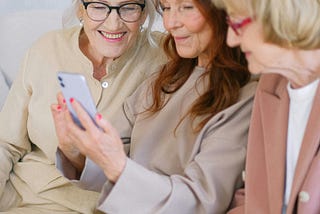 3 older women sitting together looking at something on a cell phone and smiling