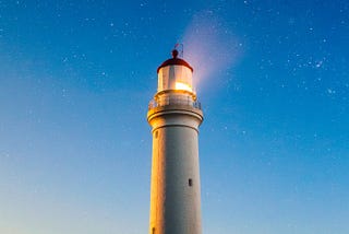 A lighthouse shines bright toward a sky of stars.