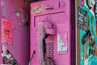 An old payphone that is spray-painted pink with grafitti and stickers all over it.