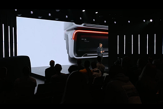 A conference screen displaying a small section of a vehicle. In front of the screen is Robert Falck, CEO Einride. In the foreground is the silhouette of the audience.