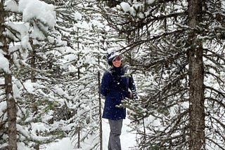 Leigh-Anne is standing among snow covered pine trees.