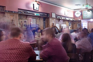 A slightly blurred picture showing a crowd of people seated in a pub.