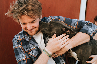 A man hugging his dog, who is kissing him