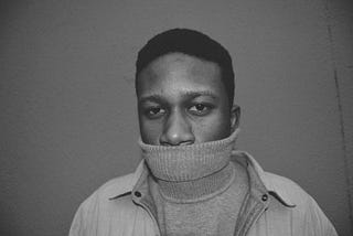 Grayscale photograph of a man wearing a turtleneck sweater pulled over his mouth.