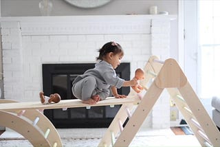 A child is sitting on a Pikler Triangle with ramp