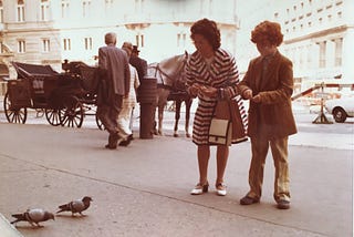 A sepia-toned photograph of a young woman and her son kneeling before some pigeons, preparing to feed them