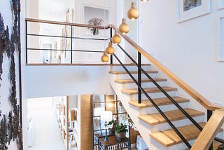 A white room with wooden accented stairs leading down to a sitting room below.