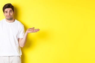 A clueless looking man in a white t shirt, shrugging and looking puzzled as if he has no idea what is going on. Bright yellow background.