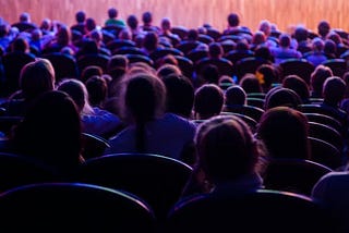 view from behind of people sat in a theatre waiting for a performance to begin