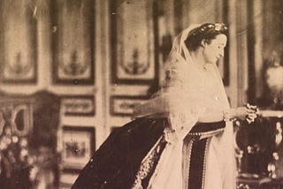 Empress Eugenie in her palace of St. Cloud, wearing a crinoline gown and a white veil.