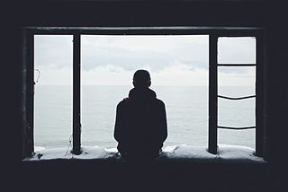 A solitary figure, seen in silhouette, sits on an open windowsill.