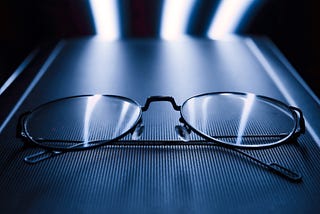 Close up of thin black eyeglasses frame on a dark blue surface with LED lights in the back.