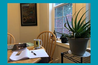A warmly lit kitchen with the blank page of a notebook, houseplants, and the bedraggled raven coffee cup.