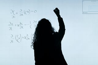 woman standing at white board writing out a formula with a marker