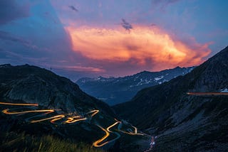 Sunset behind a mountain with a lit up winding road heading down the mountain