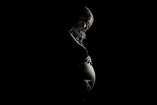 Pregnant young woman looking down at her bump which she is cradling with her hands.