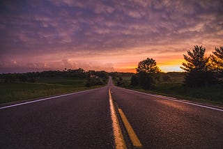 An empty road in between grass fields at dusk