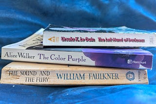 Stack of three paperback books: The Left Hand of Darkness by Ursula K. Le Guin, The Color Purple by Alice Walker, and The Sound and the Fury by William Faulkner.