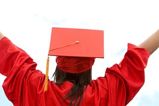 a persona in the graduation cap and gown faces away from the camera with hands and arms up in the air in celebration