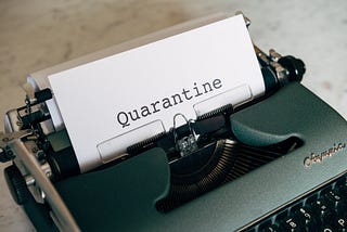 Old typewriter with sheet of paper in the roll, where the word ‘Quarantine’ has been typed.