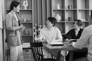 Grayscale Photo of a Woman Talking to Her Colleagues