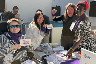 A photo of WEI’s exhibition booth at the Global Disability Summit. In the photo different people who showed up, some with physical disabilities and mobility devices, some without. They are wearing purple bandanas to show themselves as feminists with disabilities. Some of them are holding cards that read The future of Gender Equality is Inclusive with WEI’s illustrations and logo.