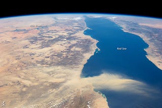 A photo from space looking onto the Red Sea from the south. The west coast of Yemen and the east cost of Sudan and Egypt are visible. The Red Sea and Nile River are labeled and one can see the mouth of the Suez in the distance. A massive dust storm is passing across the southern third of the image.