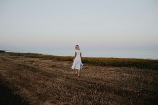 A woman in a white dress stands in a meadow.