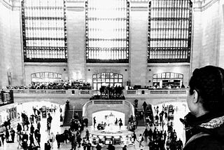 Woman on foreground looking at Grand Central Station’s main foyer in background. Black and white.