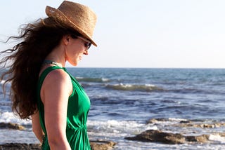 A contented looking woman at the beach wearing a green dress