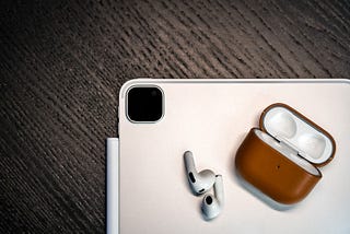 An iPad and a pair of AirPods Pro resting on a wooden table.