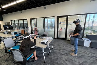 Three people using VR headsets, their faces covered and their hands gesturing in the air to interact with the virtual world they are experiencing